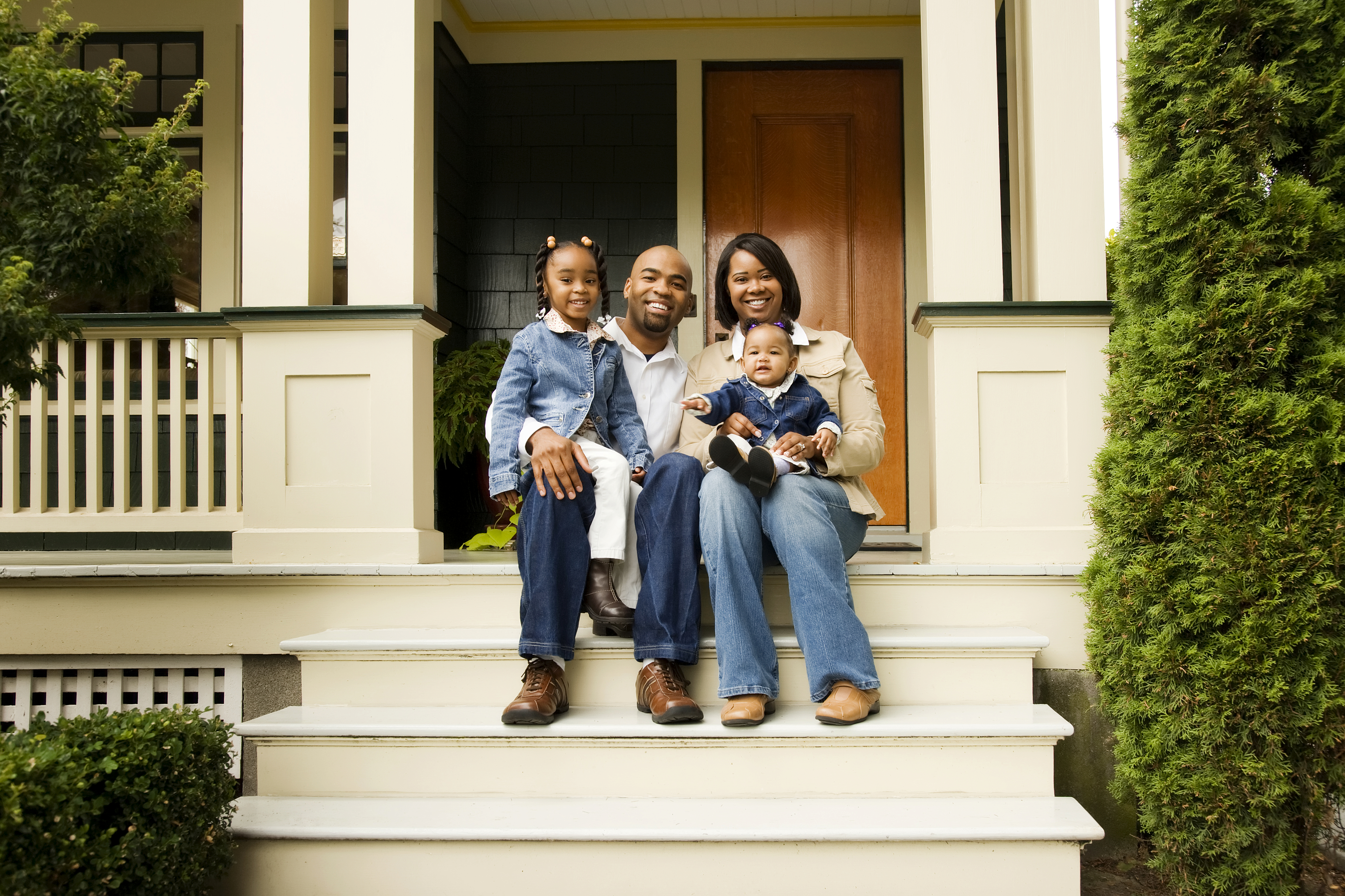 Une famille avec une jeune fille et un bébé assis sur le porche d'une maison.