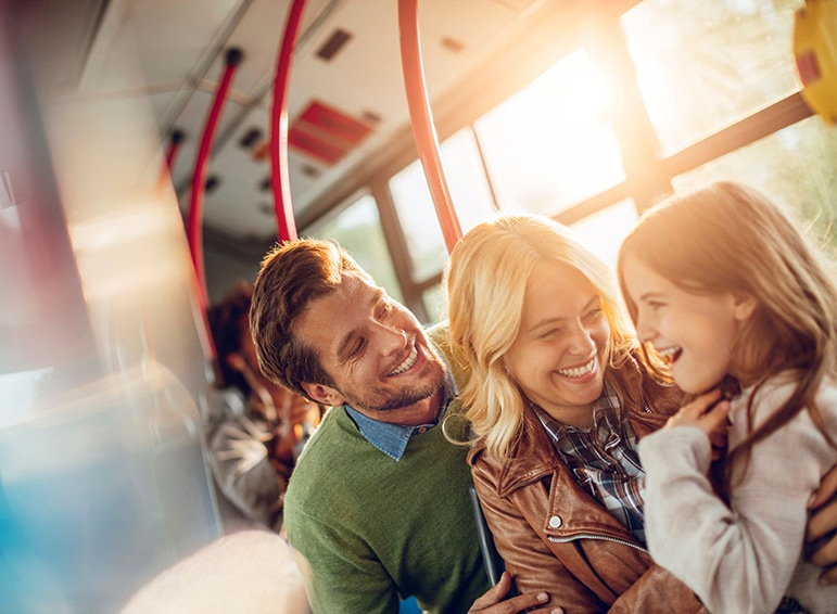 Une famille souriante et riante, assise dans le bus avec un arrière-plan lumineux et ensoleillé.